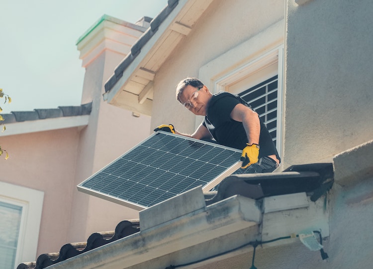 uomo sul tetto di una abitazione intento ad installare un pannello solare per iniziare a produrre energia elettrica col tetto di casa
